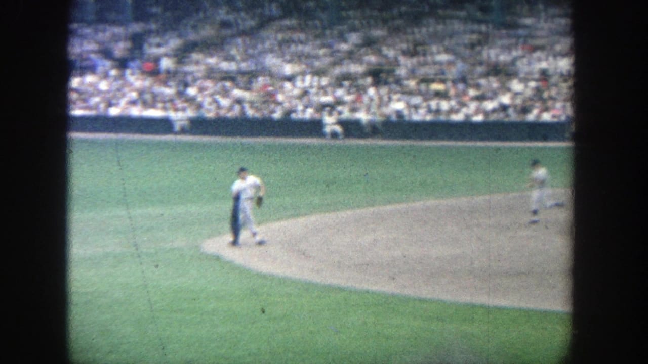 1964 Yankee Stadium frame showing a baseball player in a white uniform crossing the infield dirt before the crowded stands.