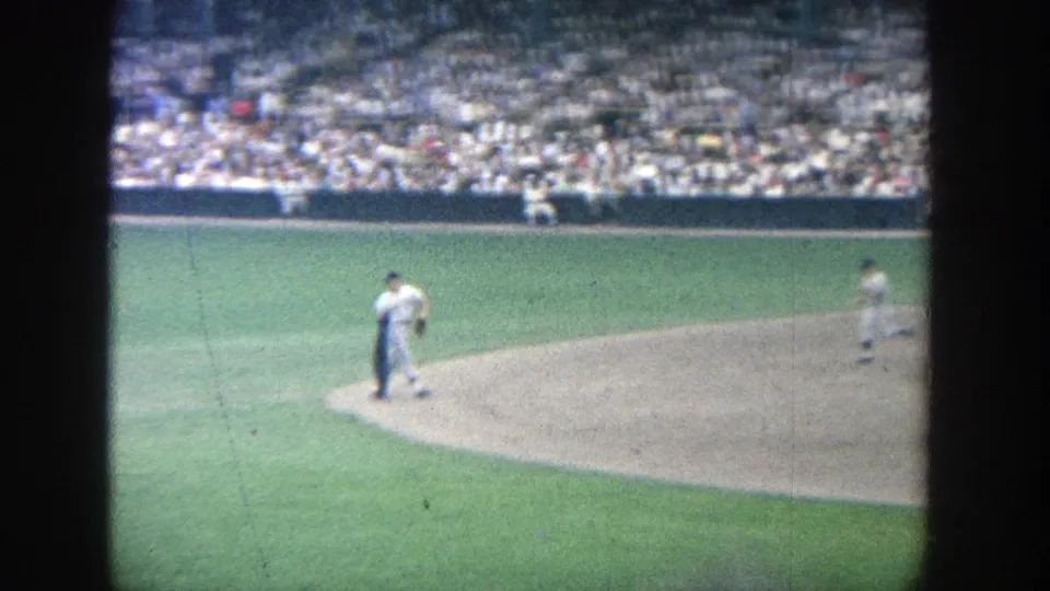1964 Yankee Stadium frame showing a baseball player in a white uniform crossing the infield dirt before the crowded stands.