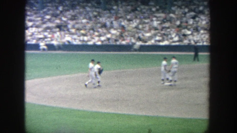 1964 Yankee Stadium frame showing a small group of uniformed players on the infield with a crowded grandstand in the background.
