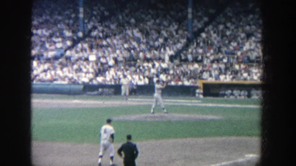 1964 Yankee Stadium frame with a pitcher near the mound, other figures on the field, and a large seated crowd in the background.