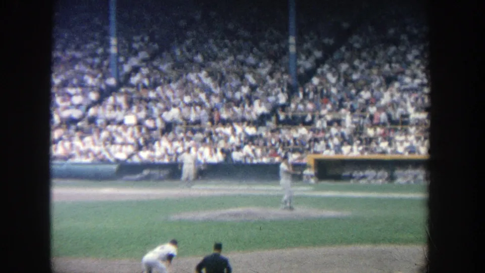 1964 Yankee Stadium baseball game viewed from the stands, with players on the field and a large crowd behind them.