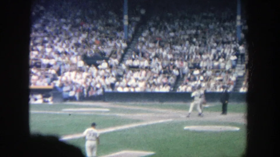 1964 home-movie view of a Yankee Stadium baseball game, with batter and umpire near the plate and spectators in the stands.
