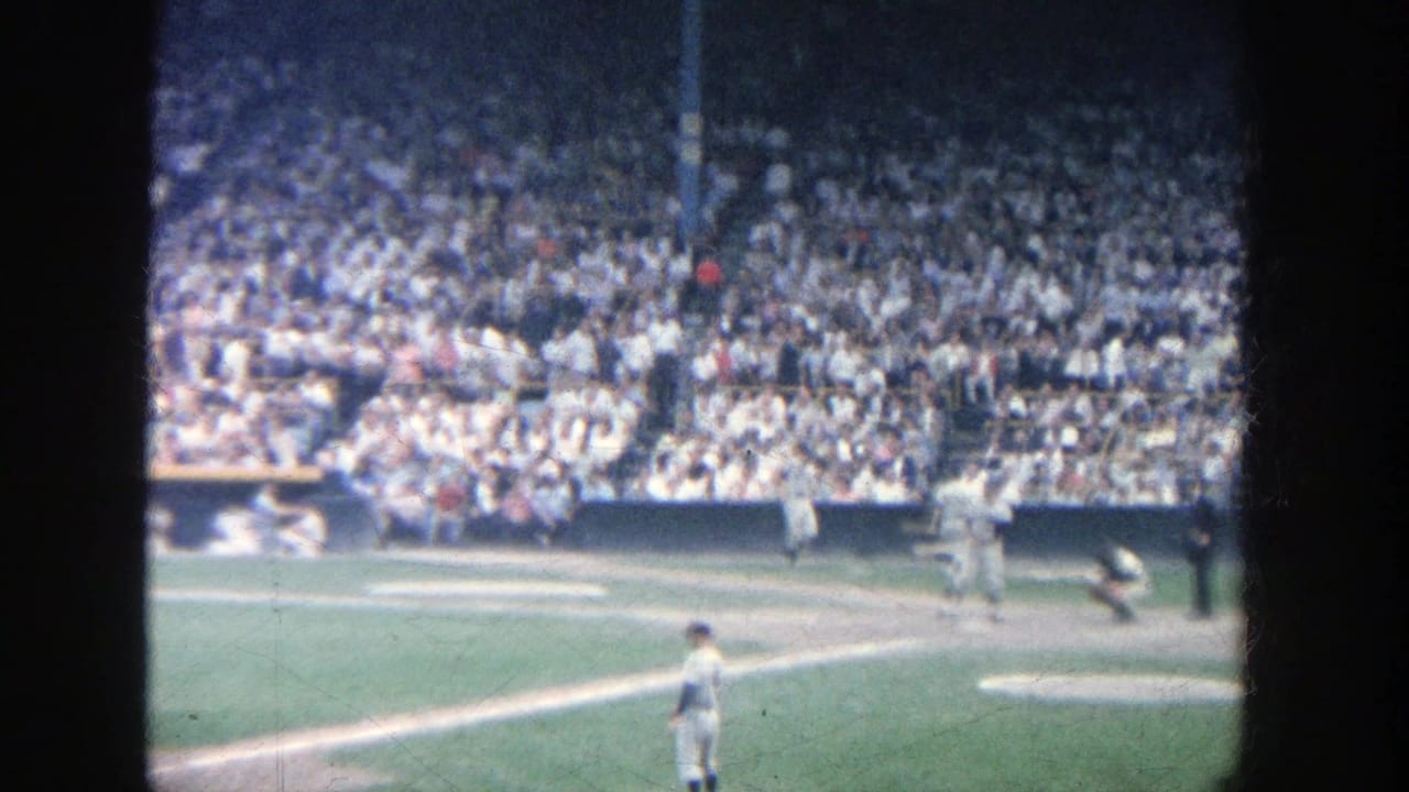 1964 8mm home-movie view of a baseball game at Yankee Stadium, with a batter near home plate and a crowd filling the stands.