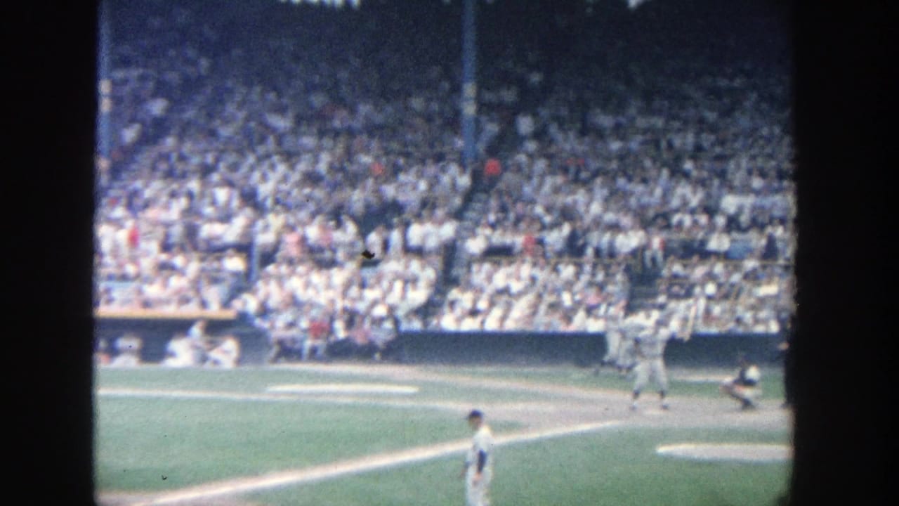Baseball batter, catcher, and nearby fielder appear on the field before a full grandstand.