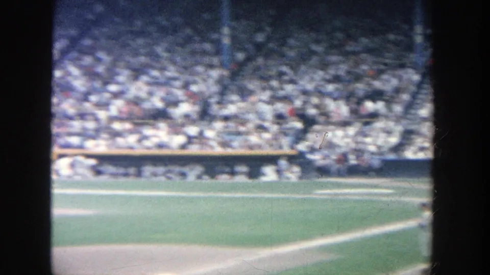 Handheld 1964 Yankee Stadium home-movie frame with the infield, home plate area, and sunlit grandstands partly visible.