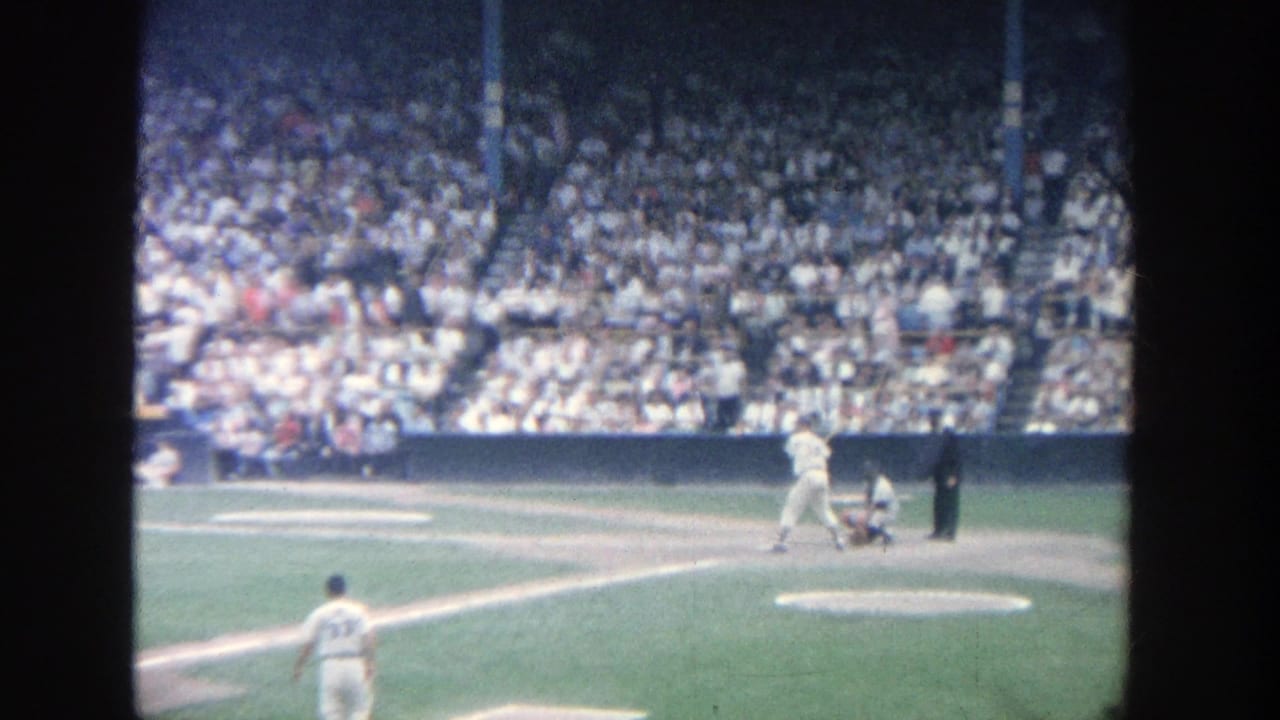Batter stands at the plate with catcher and umpire behind, seen from the stands.