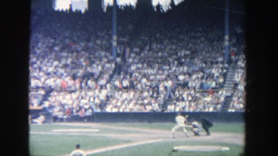 Late frame from the 1964 Yankee Stadium clip showing the batter near home plate, catcher and umpire behind, and spectators filling the stands.