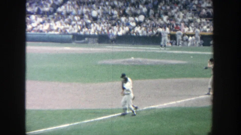 1964 Yankee Stadium frame with a player walking along the baseline and other uniformed players near the dugout.