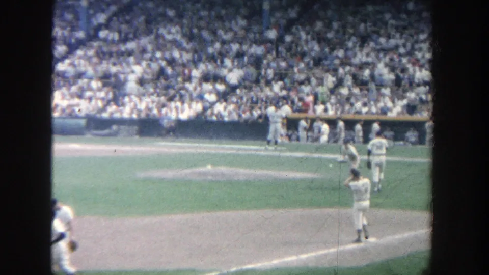 1964 Yankee Stadium home-movie view of players on the field near the baseline, with dugout activity and packed stands beyond.