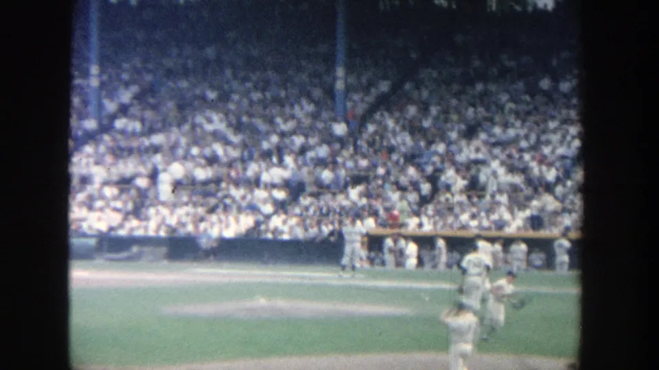 1964 Yankee Stadium frame showing players crossing the infield area in front of crowded spectator seating.