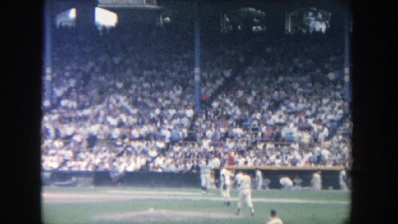 Baseball players move near the mound and infield as spectators fill the stands.