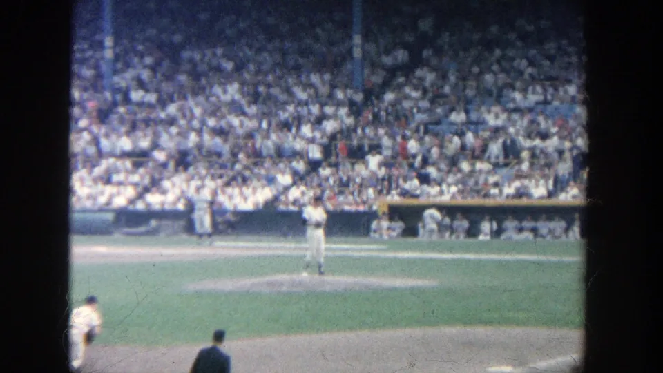 Home-movie view of a 1964 Yankee Stadium baseball game, centered on the mound with players and packed stands behind it.