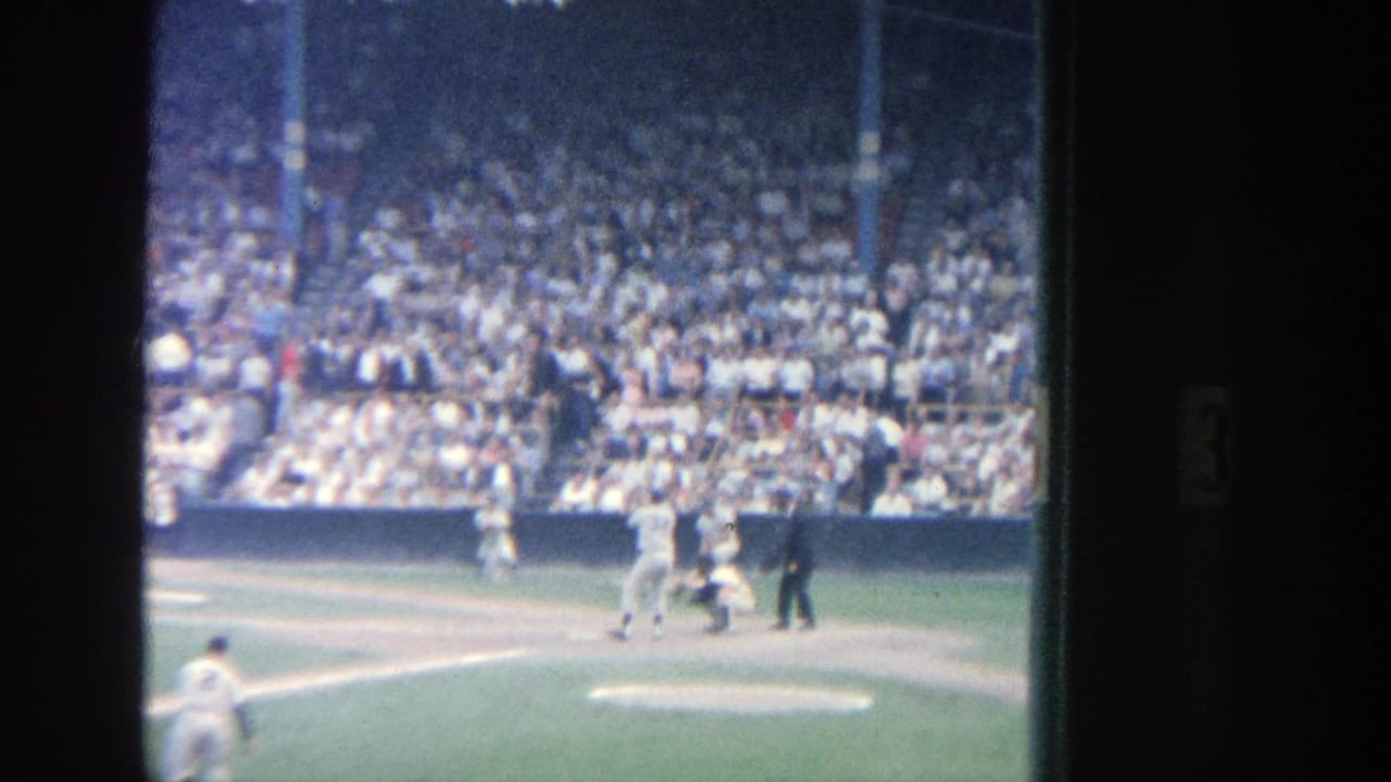 Batter near home plate with catcher, umpire, and crowded stands behind.