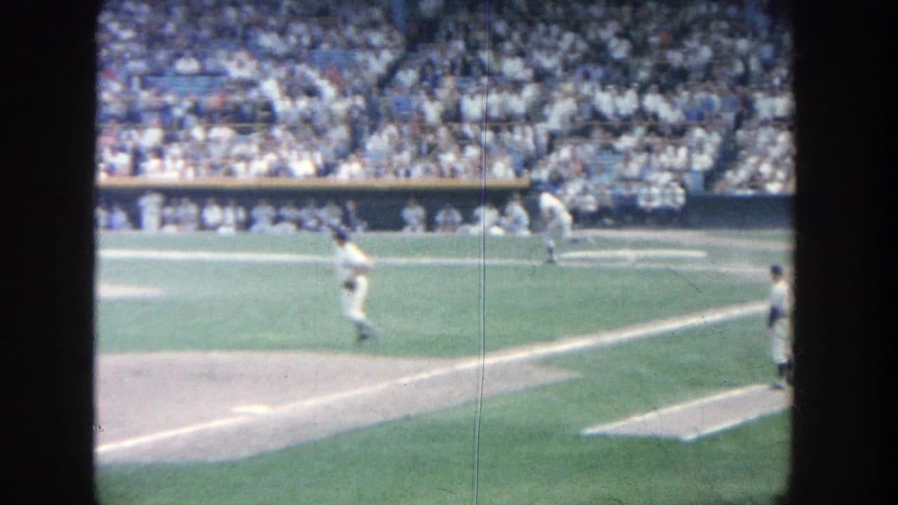 Baseball infield with pitcher area, baserunner, and spectators in the stands.