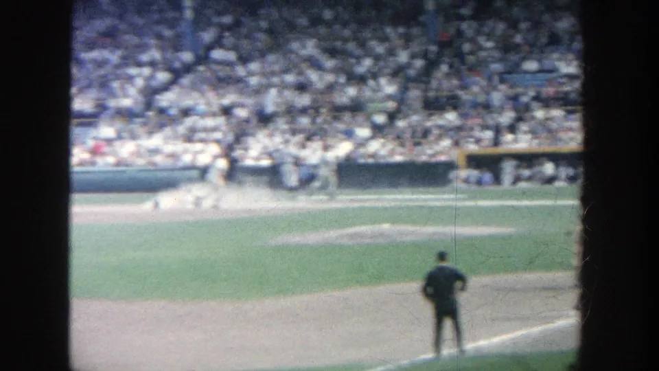 1964 Yankee Stadium frame showing infield movement near a base, an umpire in the foreground, and spectators across the stands.
