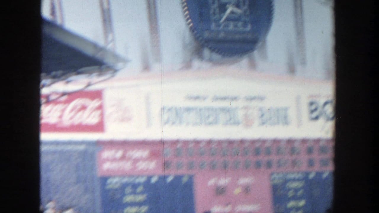 Soft 8mm frame of the Yankee Stadium scoreboard area, with blurred Longines clock, Coca-Cola sign, and distant spectators.