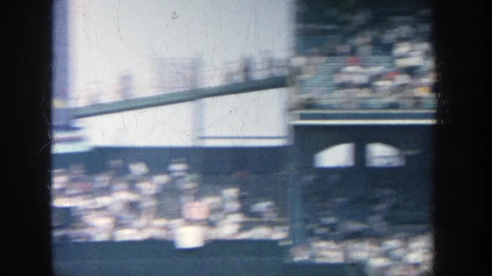 Motion-blurred 1964 Yankee Stadium view across spectators, railings, and stadium architecture with strong exposure changes.