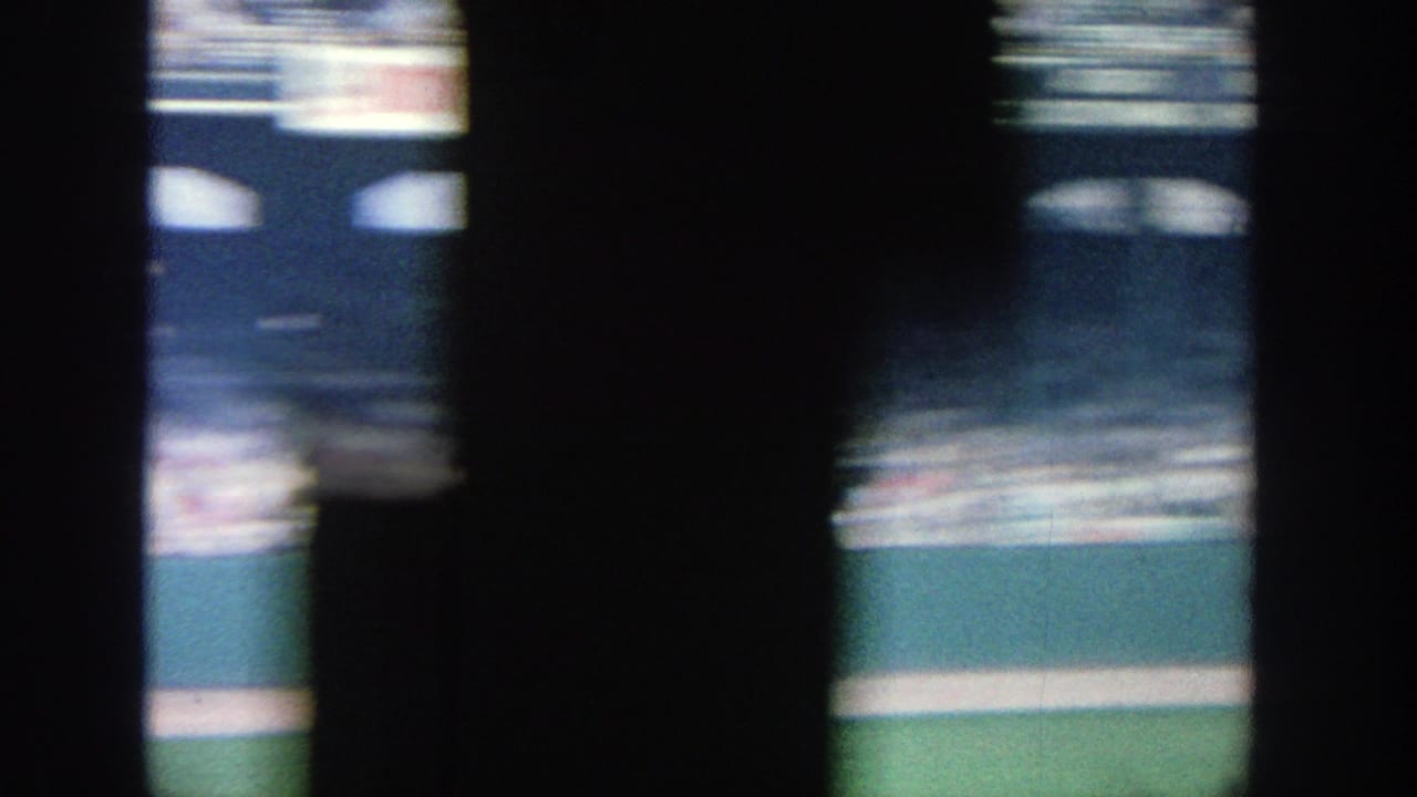 Late frame from the 1964 Yankee Stadium pan, with crowded seating, dark foreground shapes, and a visible green field edge.