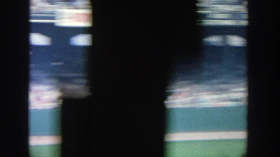 Late frame from the 1964 Yankee Stadium pan, with crowded seating, dark foreground shapes, and a visible green field edge.