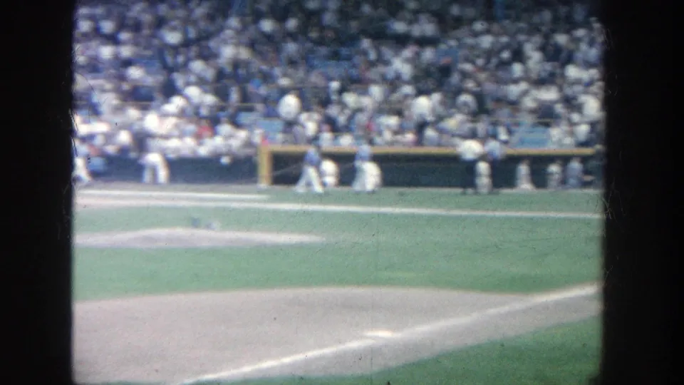 1964 Yankee Stadium view toward the dugout and infield edge, with players near the bench and crowded stands in soft 8mm focus.
