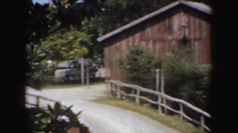 Rural California carriage-route frame from 1952 showing a barn, white fence, trees, road, and a partly hidden parked car.