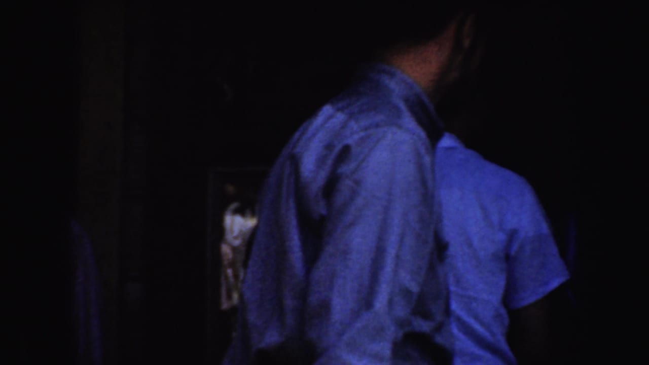 Men in light shirts stand or pass near a dark entrance.