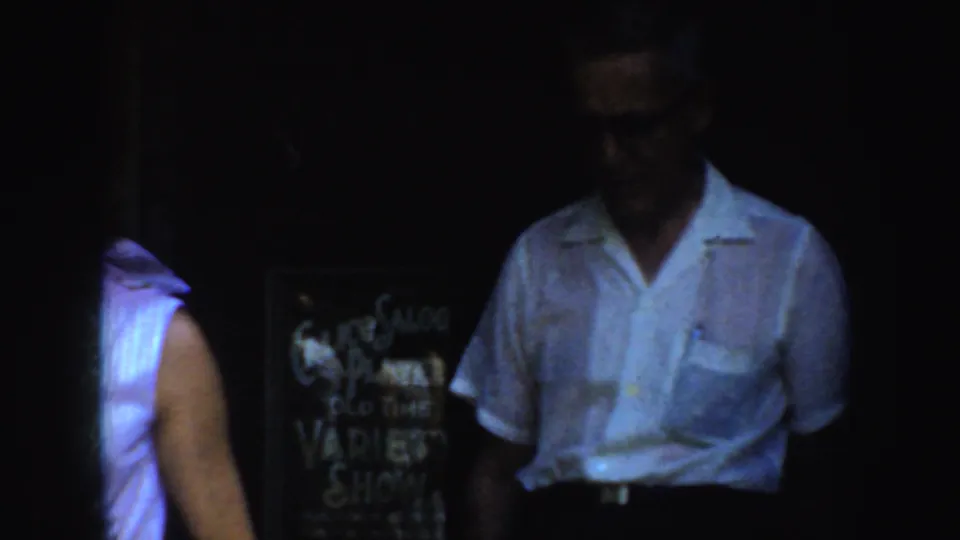 1952 California 8mm frame showing a man in glasses beside the saloon variety show sign in a dark doorway setting.