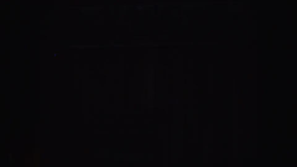 Underexposed home-movie frame with shadowy vertical forms and slight blue-red flare in the darkness.