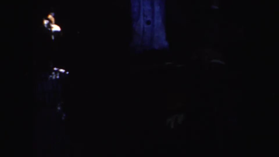 Underexposed 8mm frame from the 1952 California clip with a blue-lit vest area and small light at left.