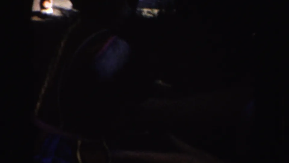In a dark 1952 California home-movie frame, a seated woman appears to handle blue fabric while wearing a white sleeveless shirt.