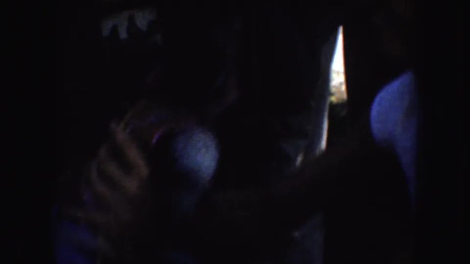 The woman remains mostly in shadow as she looks down and handles a blue object or garment in the 1952 California footage.