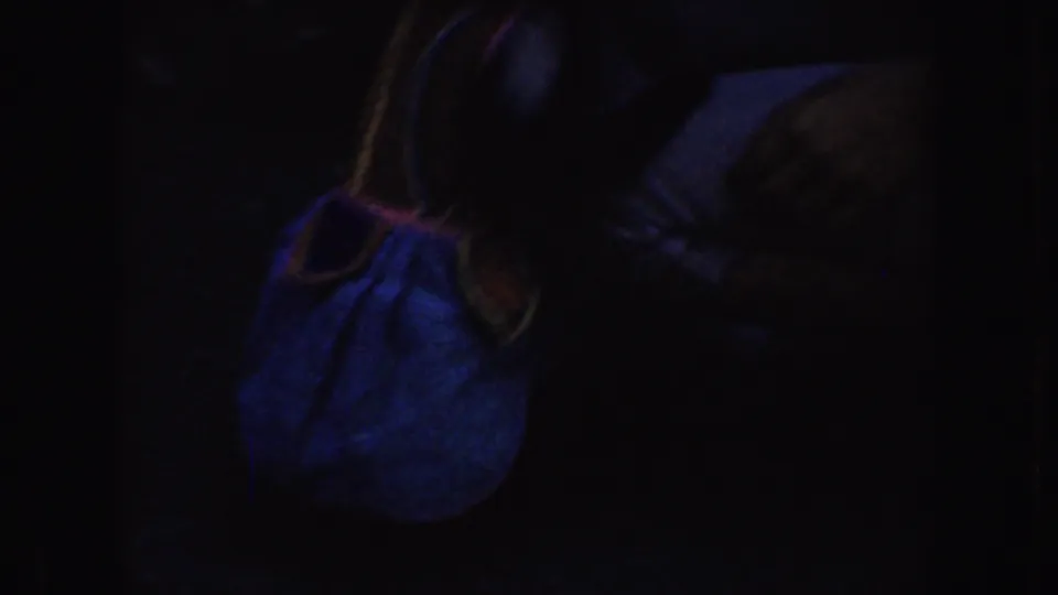 A dim 8mm frame shows the woman leaning toward a blue garment or object with a yellow-trimmed edge in her lap.