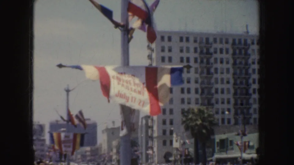 1952 California street scene with fluttering flags, a partly turned pageant banner, palm tree, and spectators below.