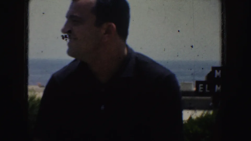 A man in a dark shirt appears in profile near a bright waterfront or distant horizon in the California home-movie footage.