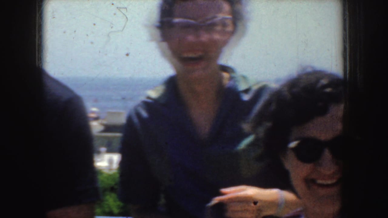 Adults laughing toward the camera near a bright ocean backdrop.