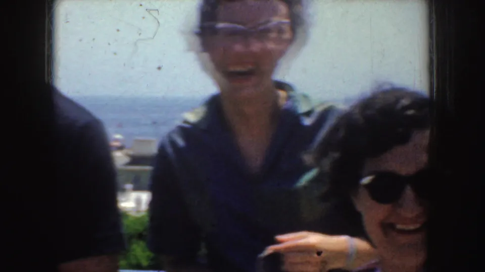 1952 California home-movie frame with adults laughing and posing near the ocean, partly cropped by handheld framing.