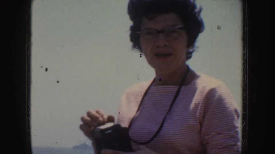 Woman in a striped top holds a small camera in a 1952 California seaside home-movie frame.