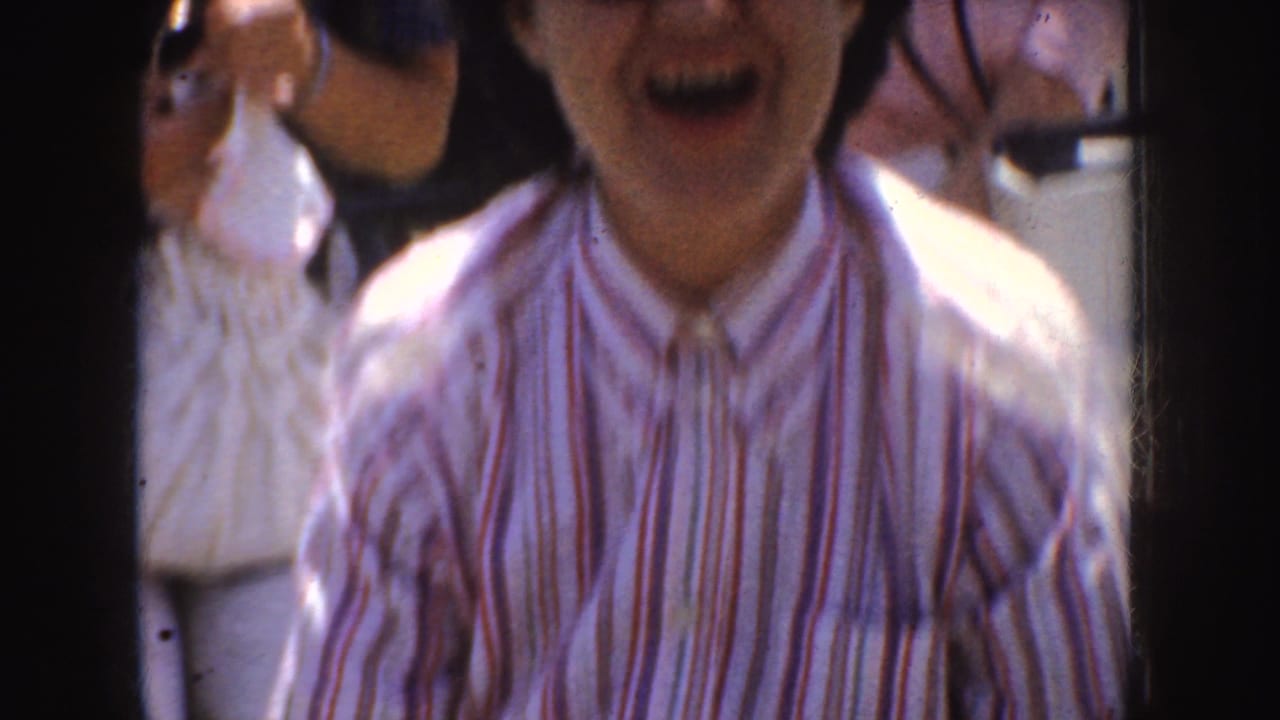 1952 California home-movie frame showing an adult in a striped shirt close to the camera, with other adults partly visible outdoors.