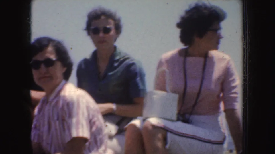 1952 California home-movie frame showing adults in sunglasses seated together outdoors on a sunny day.