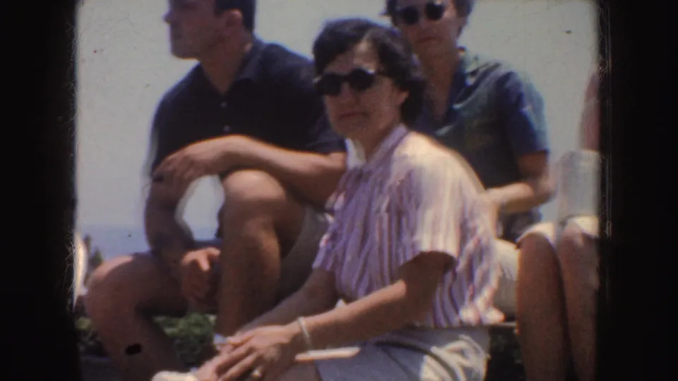 1952 California home-movie frame showing adults seated on benches, with striped summer clothing and sunglasses visible.