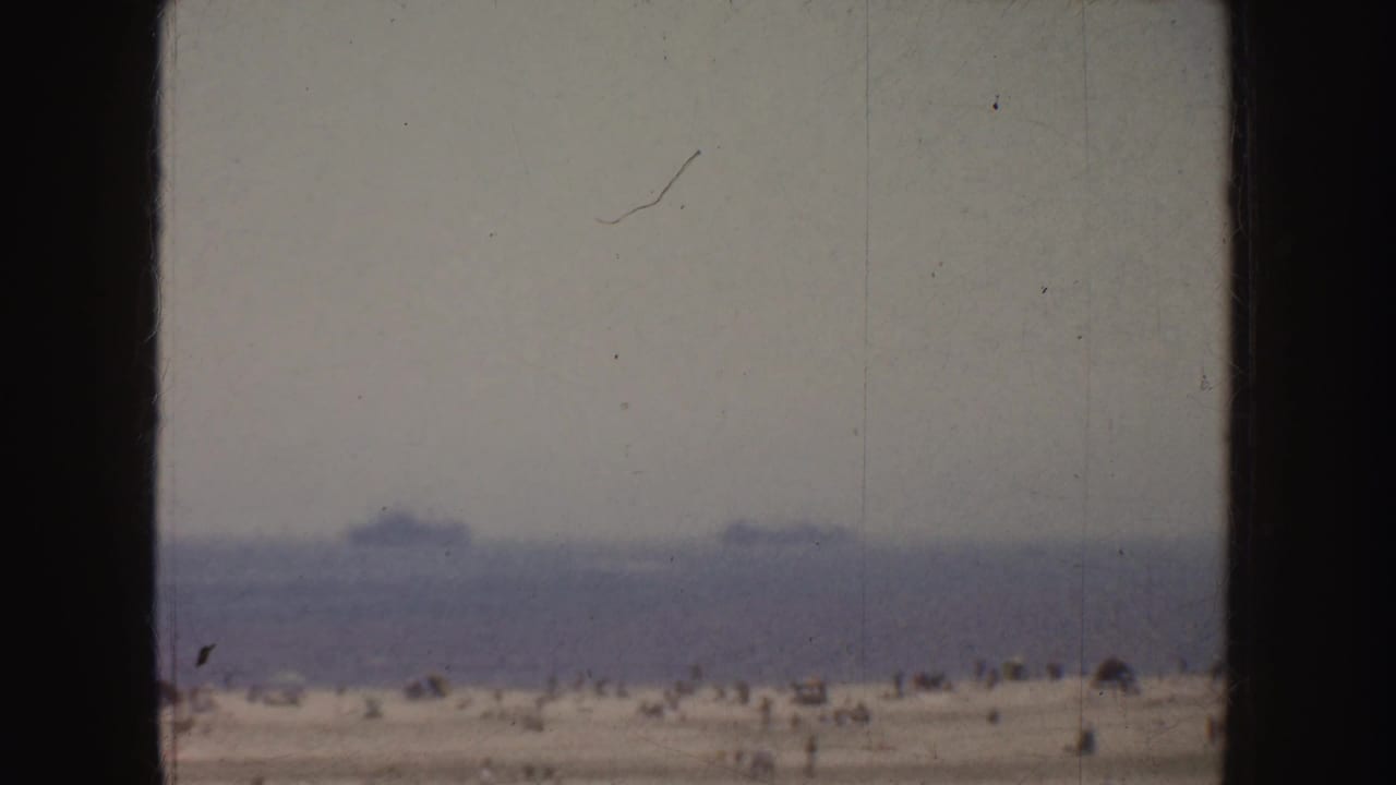Distant ships on a hazy ocean horizon above a sandy beach.