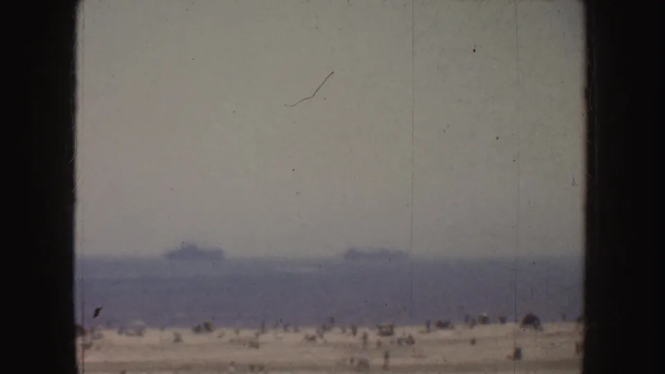 1952 California beach view with hazy ocean, distant ship silhouettes, and a partially visible beach sign near the lower edge.