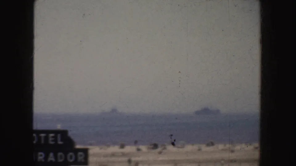 Hazy California shoreline view from 1952 with several large ships far offshore and a cropped sign in the foreground.