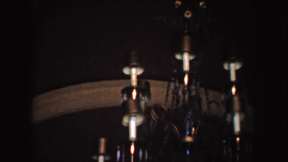 1952 California 8mm frame showing a dim interior with part of a hanging chandelier, pale bulbs, and dark surrounding surfaces.