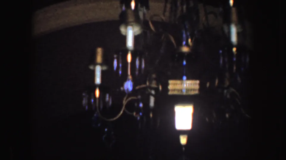 1952 California 8mm frame of a chandelier in low light, with a bright bulb and blue-toned decorative drops against a dark interior.