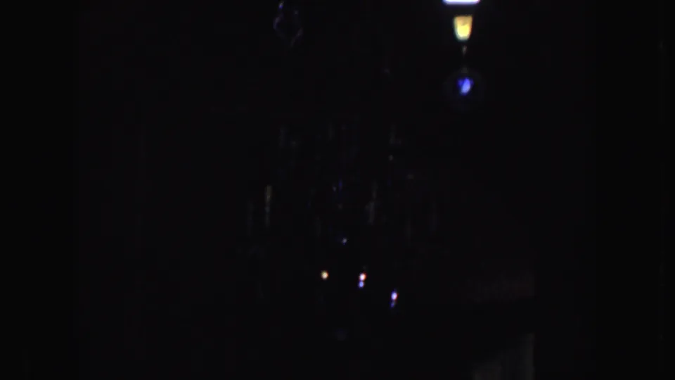 1952 California 8mm frame showing the lower, shadowed portion of a chandelier with faint reflections and dark interior space.