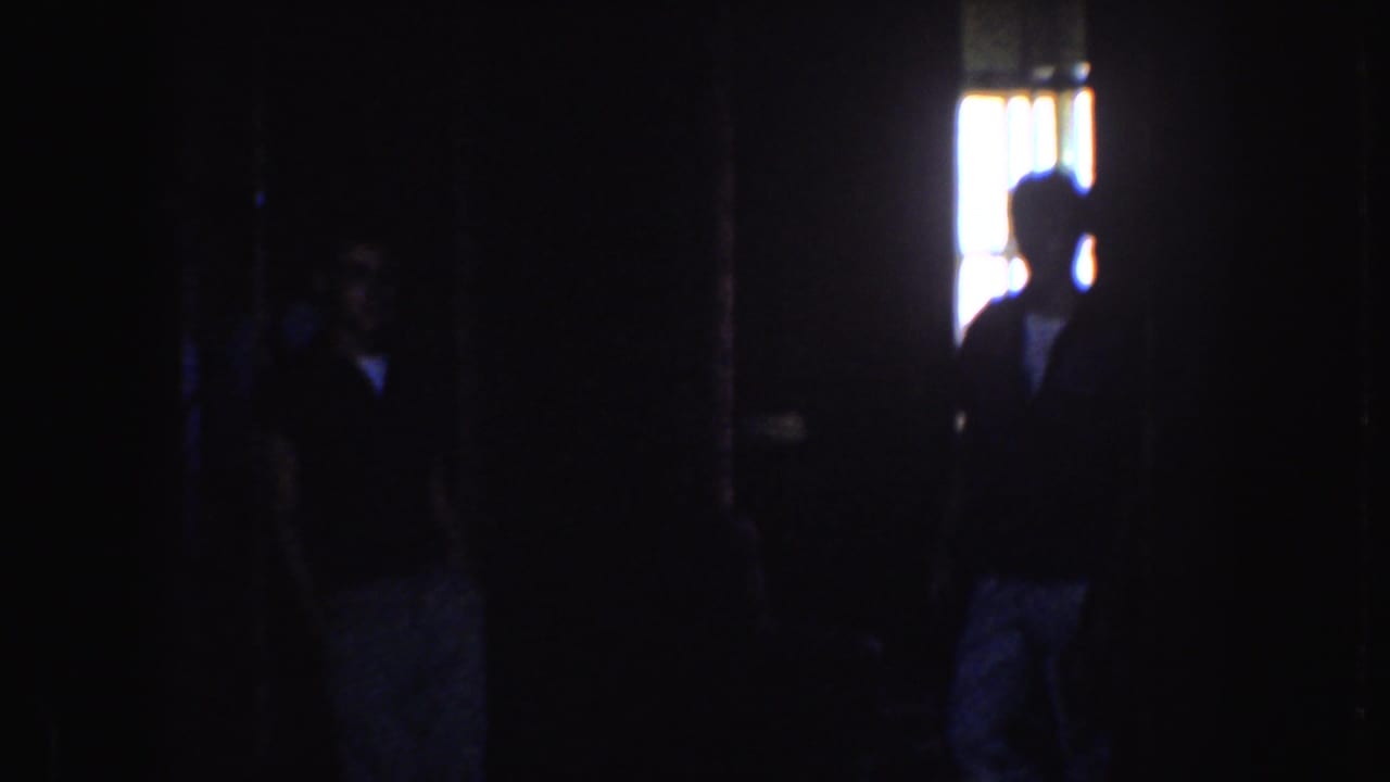 Dark interior with silhouetted figures near a bright doorway or window.