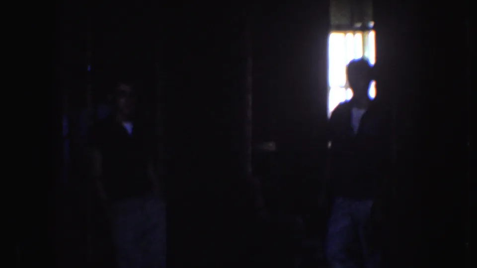 Dim 1952 home-movie frame showing silhouetted people inside or under shade, with bright daylight beyond.