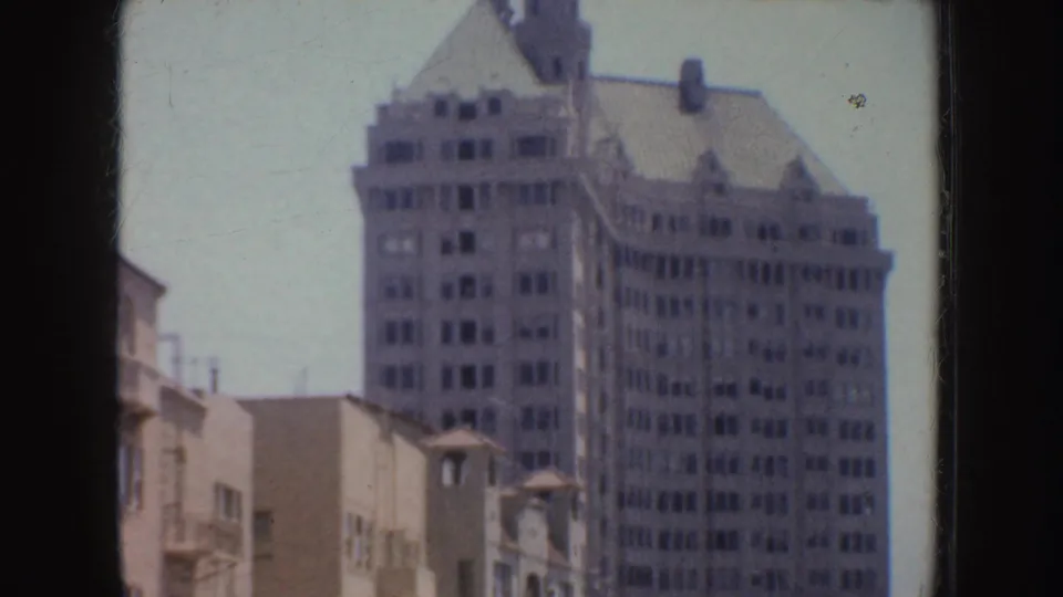 1952 California street view with a tall older building, pointed roofline, and lower pale buildings along the foreground.