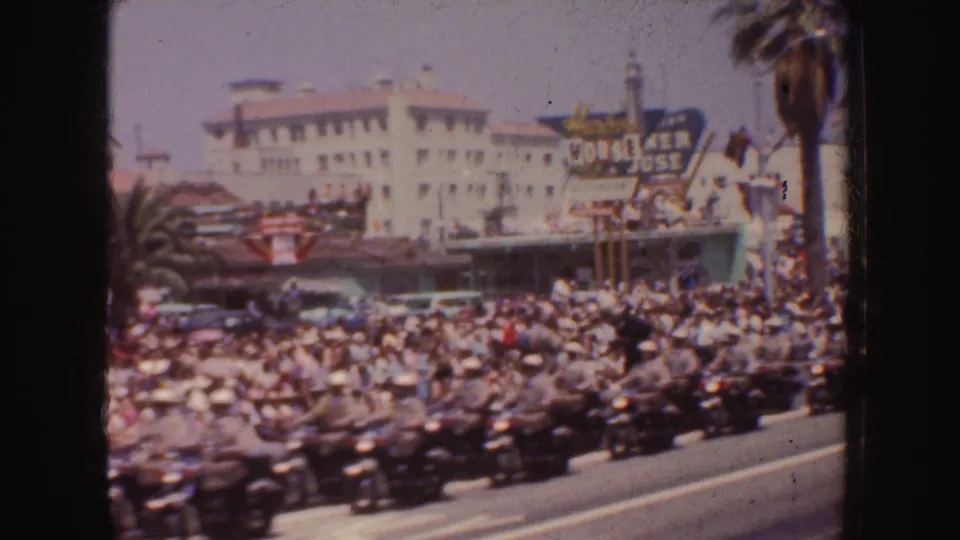Parade spectators watch motorcycles pass on a California street, with palm trees and the House of Jose sign in the background.
